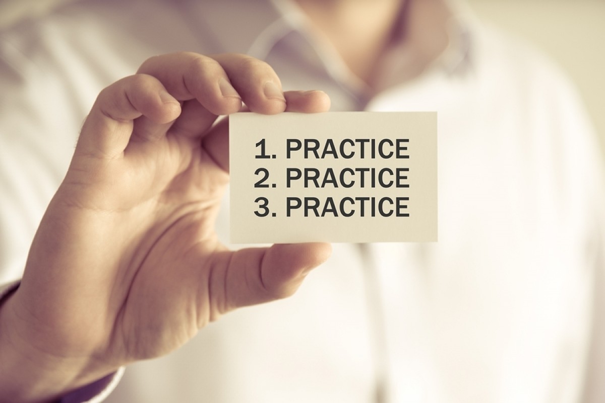 A man holding a card saying Practice, Practice, Practice!